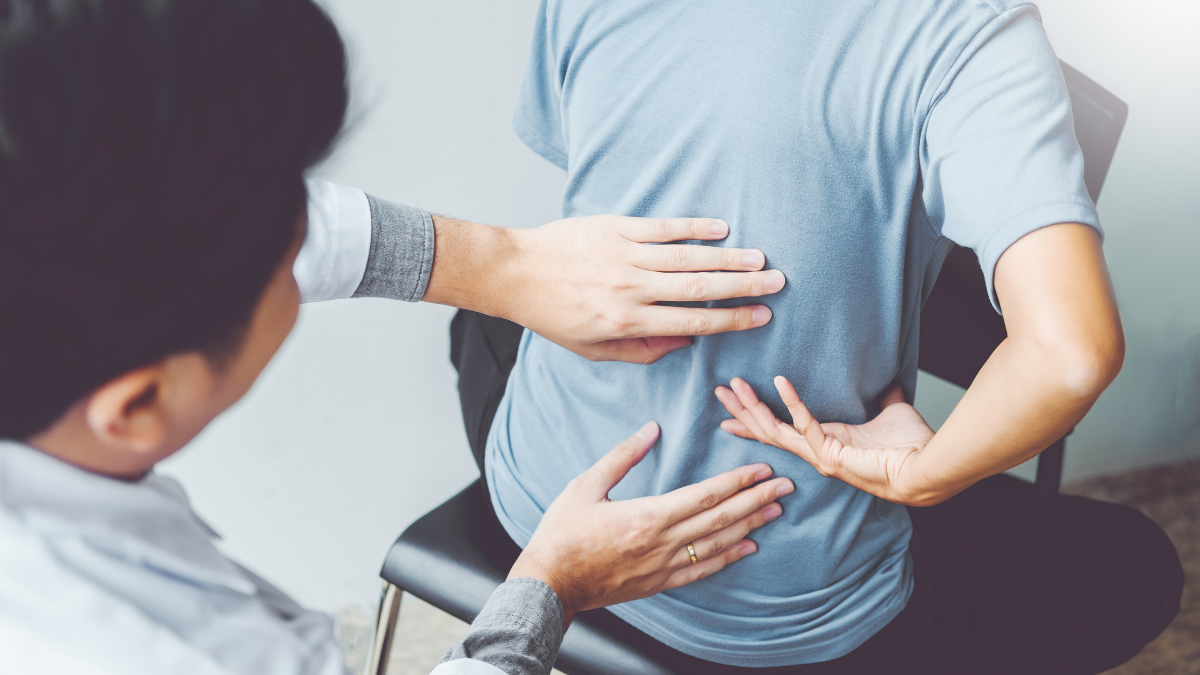A physical therapist examining the lower back of a male patient seated on a chair