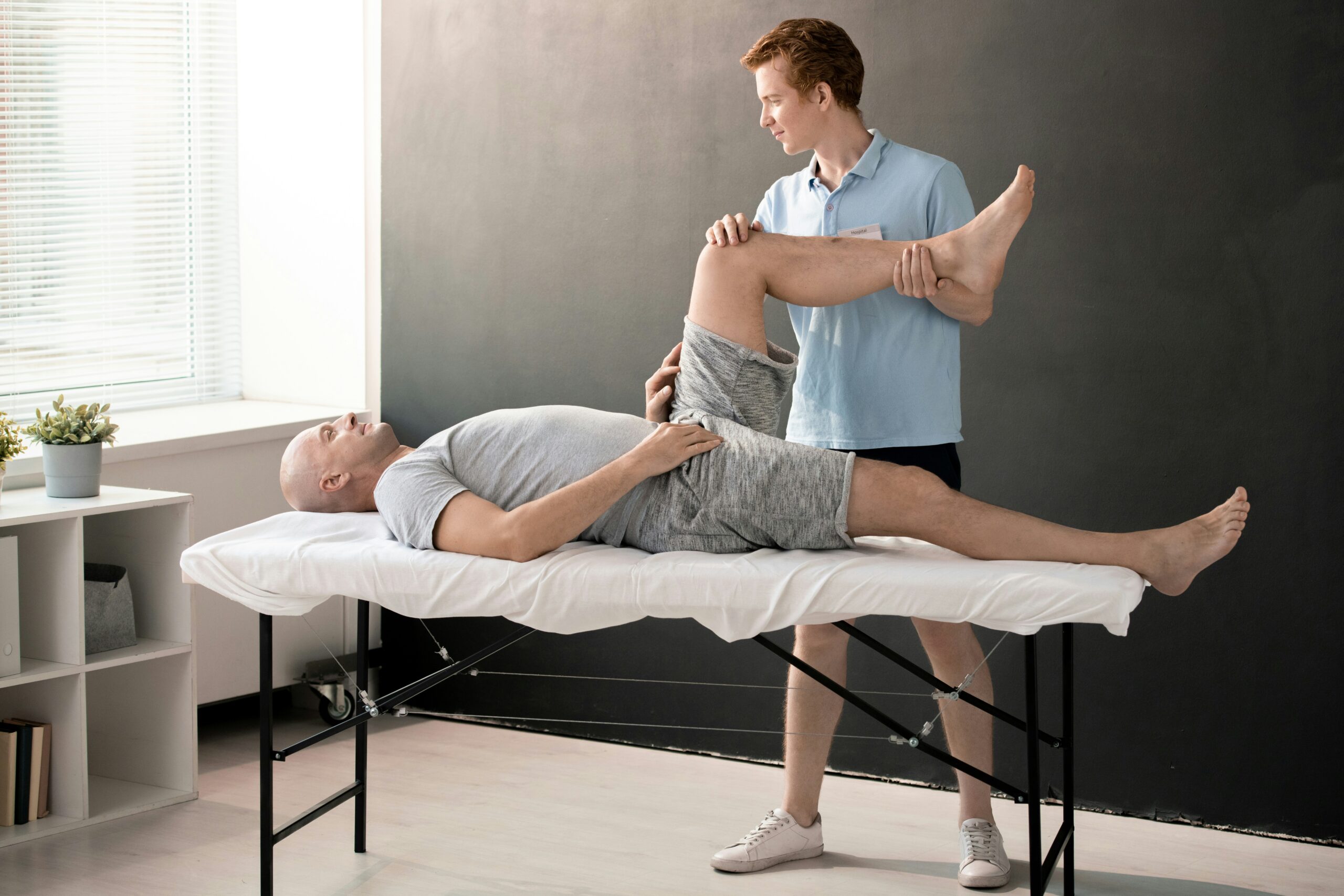 Physical therapist assisting a patient with a knee and hip mobilization exercise on a table.
